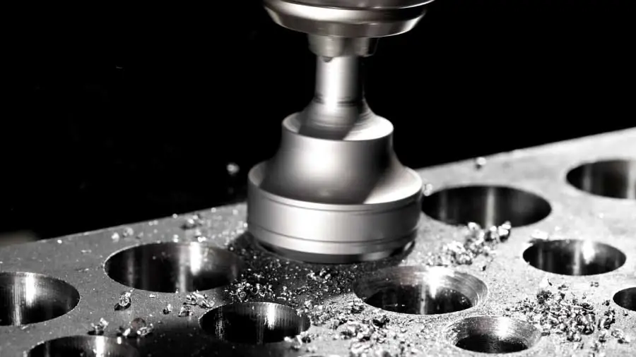 Close-up of a Poplock deburring tool in action, grinding down and smoothing out the edges of circular holes on a metal component, with visible metal shavings and sparks.