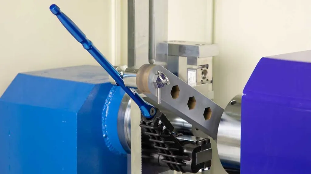 Indexing pry bar undergoing quality testing, mounted on a testing rig designed to measure torque and leverage, featuring blue and silver components highlighted against a precision machine background.